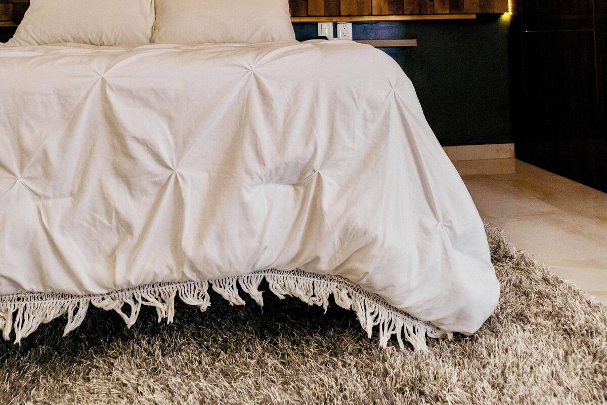 Quarto moderno com cama grande, luminária pendente e parede texturizada.