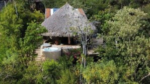 A thatched-roof house surrounded by dense greenery, with a visible swimming pool and outdoor seating area. - Casa Monte Pacifico, your haven of serenity between beach and rainforest. (San Agustinillo)