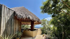 A wooden structure with a thatched roof, surrounded by various potted plants and cacti. - Casa Monte Pacifico, your haven of serenity between beach and rainforest. (San Agustinillo)