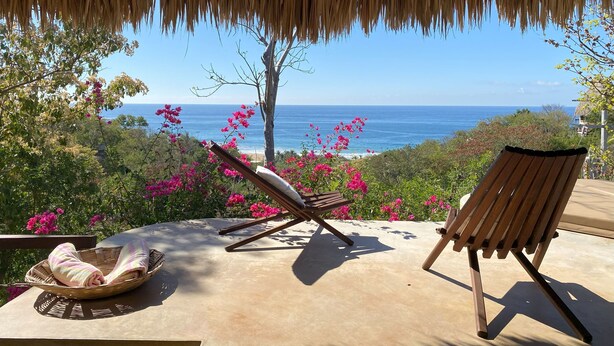 A beachside lounge with a view of the ocean, a thatched roof, and a wicker basket with towels. - Casa Monte Pacifico, your haven of serenity between beach and rainforest. (San Agustinillo)