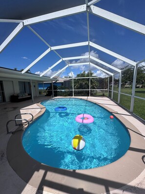 A covered swimming pool with clear blue water, metal pool ladders, and inflatable rings.