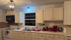 A kitchen with white cabinets, a microwave, a stove, a sink, and various appliances including a red coffee maker and a blender. - Charming 2-bdrm home in Little Rock with WiFi and AC (Little Rock)