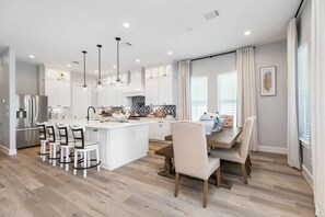 A modern kitchen with white cabinetry, a central island, and pendant lighting. - Serenity Cove Beachside Village Galveston - Lux 4bd Sleeps 12 w/ Beach Access (Galveston)