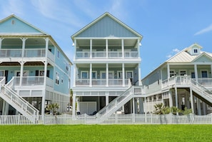 A beachfront property with a two-story house featuring a balcony, a covered porch, and a white picket fence. - Serenity Cove Beachside Village Galveston - Lux 4bd Sleeps 12 w/ Beach Access (Galveston)