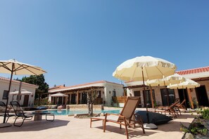A poolside area with lounge chairs and umbrellas, a swimming pool, and a building with a tiled roof. - Casa Afytos (Kassandra)