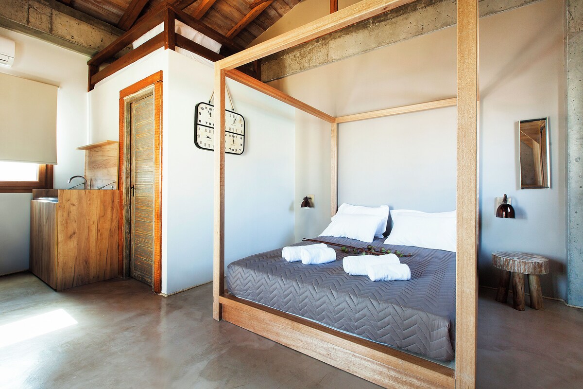 A bedroom with a wooden four-poster bed, a wooden desk, and a small round wooden stool.