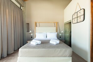 A neatly made bed with white linens and rolled towels, a wooden headboard, and a wall-mounted clock.