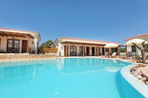 A swimming pool with lounge chairs and umbrellas, surrounded by buildings with tiled roofs and stone walls. - Casa Afytos (Kassandra)