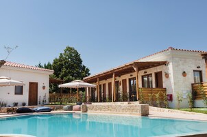 Un espace piscine avec des chaises longues et des parasols, un bâtiment en pierre avec un toit en tuiles et une pergola en bois.
