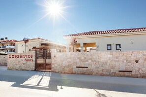 A hotel entrance with a stone wall, a sign reading "Casa Aftos Suites," and a clear sky.