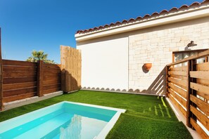 A backyard with a swimming pool, a wooden fence, and a white brick wall.