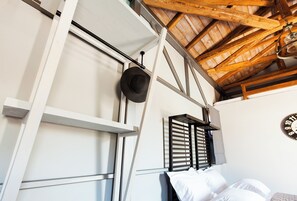 A room with a sloped ceiling, a bed with white bedding, a hat hanging on the wall, and a clock on the wall.