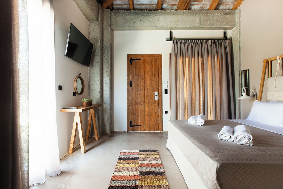 A hotel room with a bed, a television mounted on the wall, a wooden door, and a curtain.