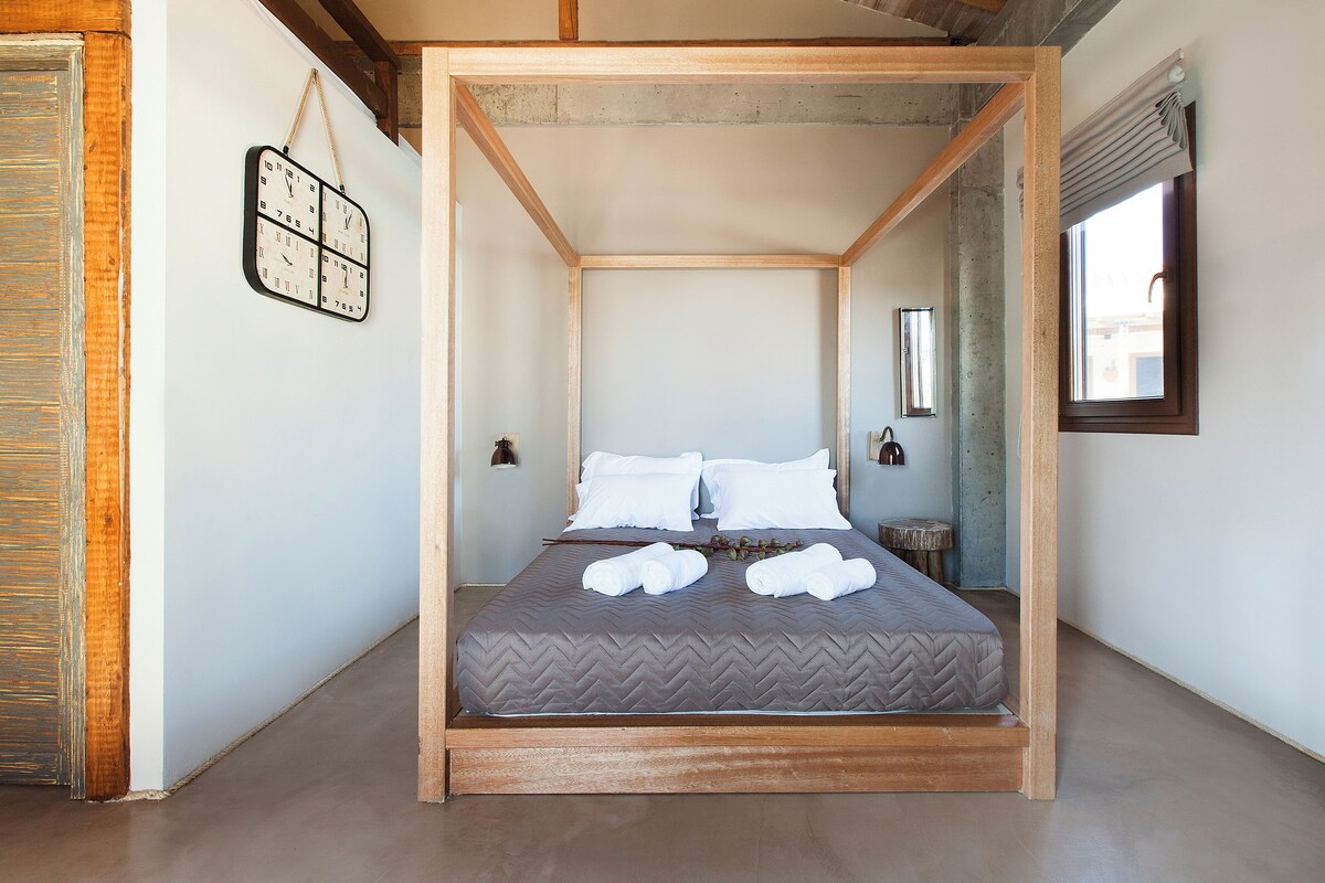 A four-poster bed with a herringbone-patterned mattress, white pillows, and neatly folded towels.