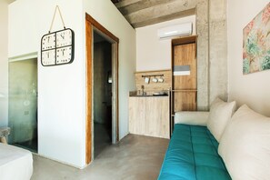 A compact living space with a kitchenette, a bed with teal bedding, and a wall-mounted clock. - Casa Afytos (Kassandra)