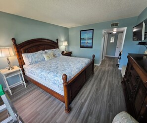 Une chambre à coucher avec un lit en bois, une table de chevet avec une lampe, une commode et un tableau accroché au mur.