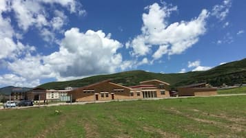 A building with a flat roof and multiple windows, surrounded by a grassy field and hills in the background.