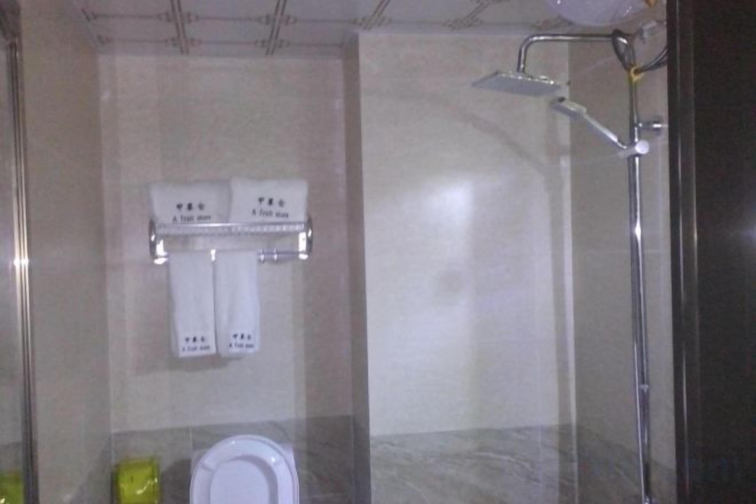 A bathroom with a toilet, a towel rack with two towels, and a shower area.