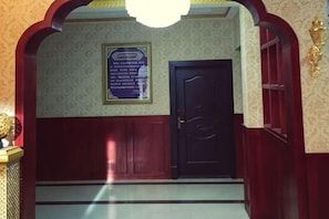 A room with a dark wooden door, a framed sign on the wall, and a chandelier.