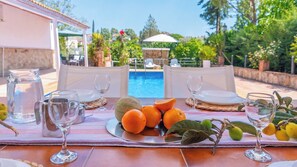 Mesa posta para refeição com vista para piscina, incluindo jarra, copos e frutas.