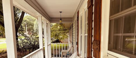 A covered porch with wicker furniture, a hanging lantern, and a view of the outdoors.