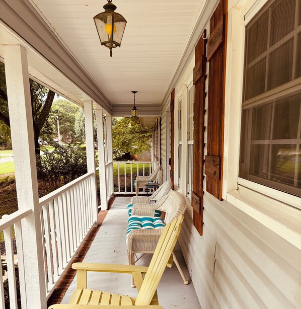 A covered porch with wicker furniture, a hanging lantern, and a view of the outdoors.