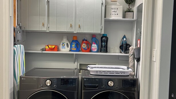 A laundry area with two front-loading washers, a shelf with detergent bottles, and a small potted plant. - The Cozy Gray House (Fort Mill)
