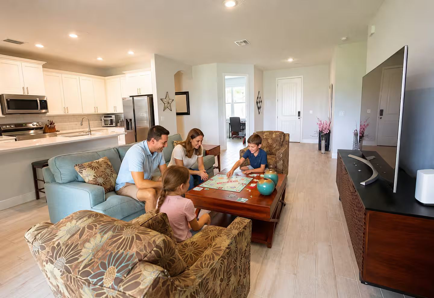 A family playing a board game in a modern living room with a kitchen in the background.