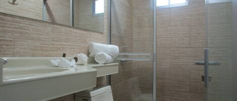 Un baño con cabina de ducha de vidrio, un lavamanos blanco y un inodoro.