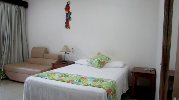Una habitación de hotel con cama, una silla, una mesita de noche y una lámpara.