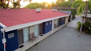 Un motel de dos pisos con techo rojo, múltiples unidades de aire acondicionado y un área de estar cubierta al aire libre.