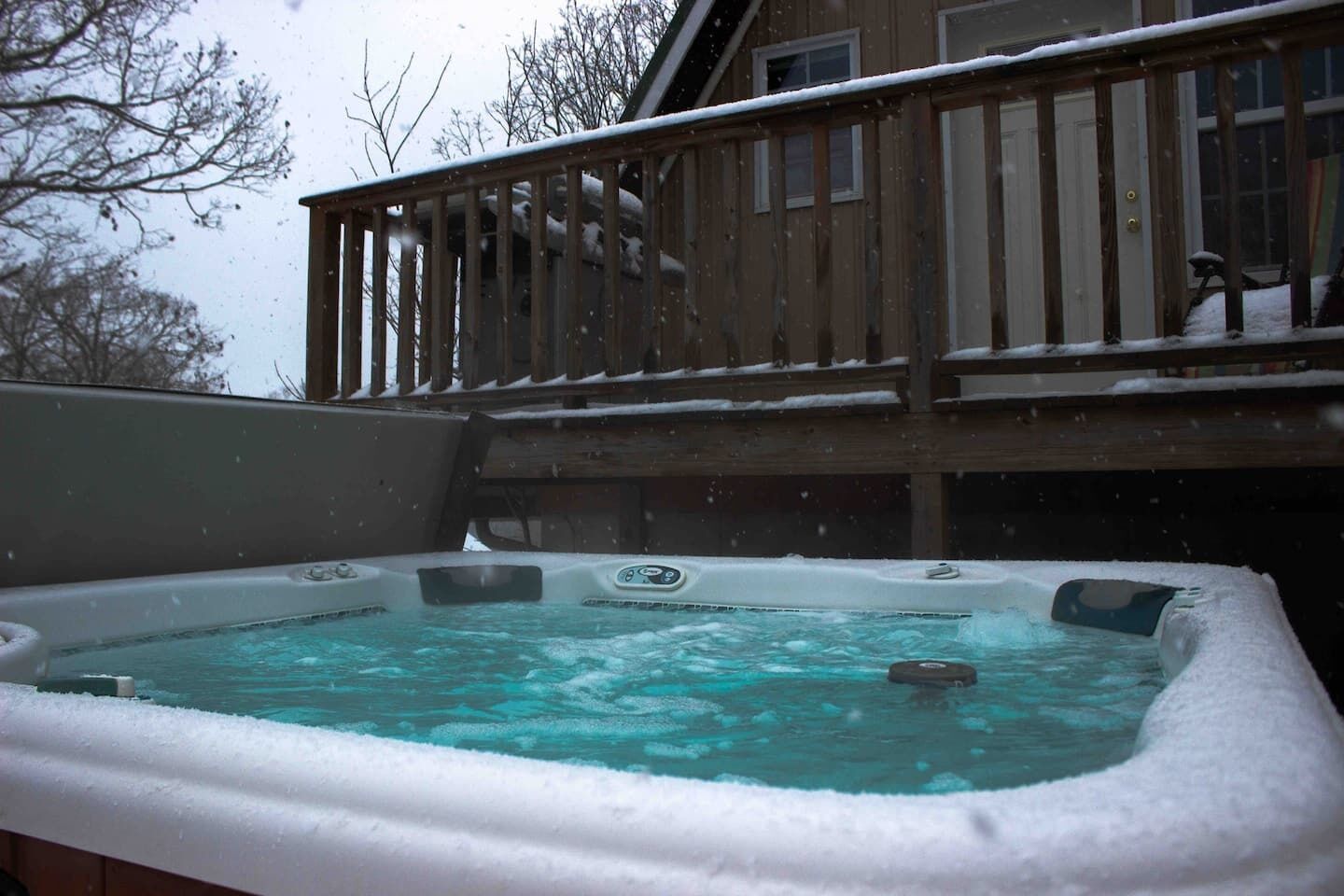 Ett bubbelbad med en trädeck och ett hus i bakgrunden.