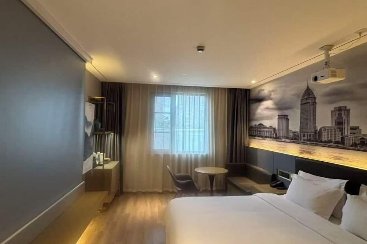 Habitación de hotel con cama, escritorio, silla, mesita y ventana con cortinas.
