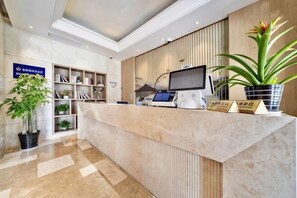 Una reception con una scrivania, un vaso di piante e un cartello.