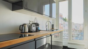 A modern kitchen with a black countertop, stainless steel appliances, and a view of the city through large windows.