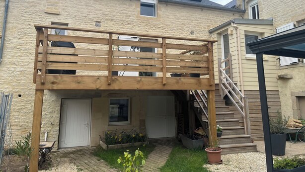 A two-story stone building with a wooden deck and a staircase leading to an upper level.