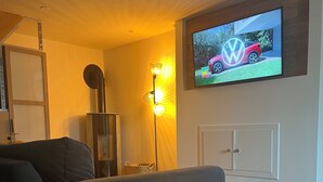 A modern living room with a grey sofa, a floor lamp, a television mounted on the wall, and a white cabinet below it.