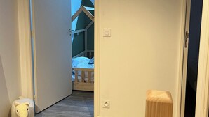 A hallway leading to a bedroom with a sloped ceiling, a wooden bed, and a small stuffed animal on the floor.