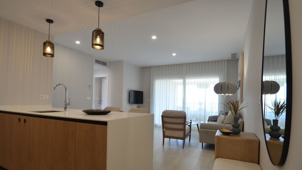 A modern kitchen with a central island, a dining area with a sofa and chairs, and a living room with a large mirror and a plant.