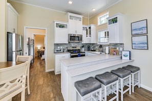 A modern kitchen with white cabinetry, a central island with bar stools, a microwave, and a stove. - Lake View Tiny Home w/ Pool Access (Sherrills Ford)