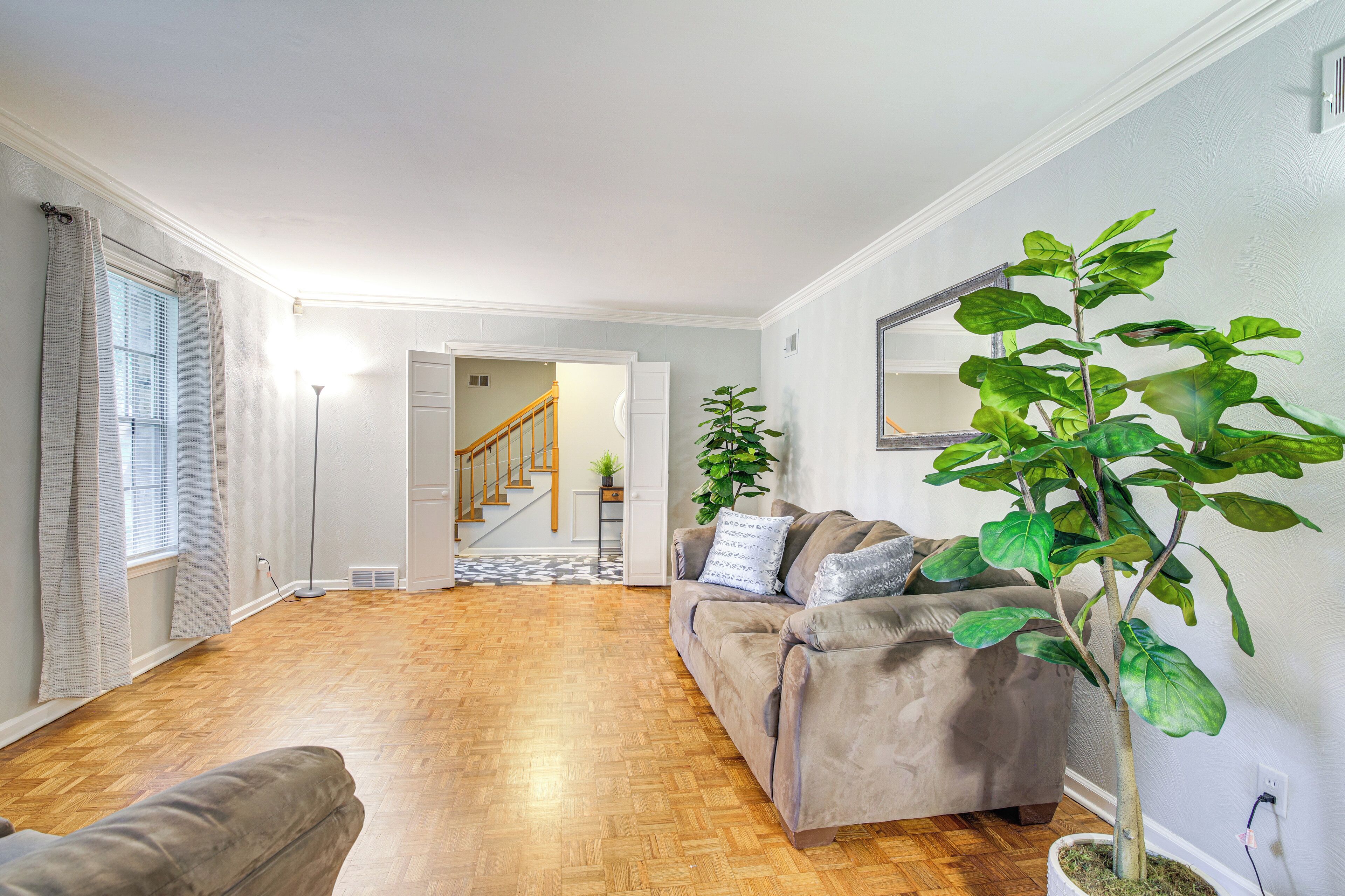 Un salon avec un plancher en bois, un canapé gris, une plante en pot et un escalier menant à une autre pièce.