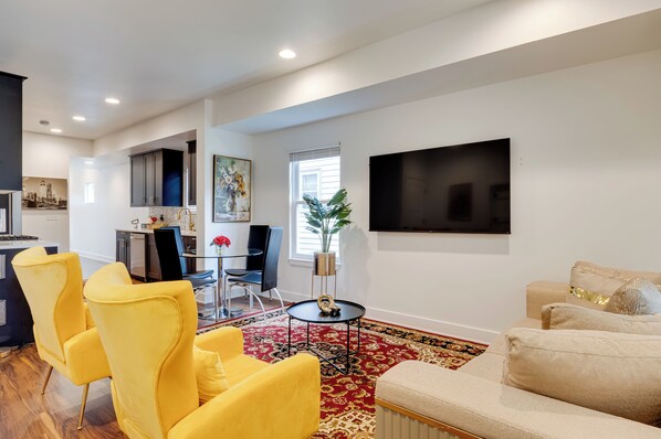 A modern living room with yellow chairs, a beige sofa, a red patterned rug, and a flat-screen TV mounted on the wall. - Walk to Parks: Dog-Friendly Gem in Indianapolis! (Indianapolis)