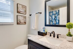 A modern bathroom with a marble sink, black faucets, a large mirror, and a blue shower curtain. - Walk to Parks: Dog-Friendly Gem in Indianapolis! (Indianapolis)