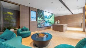 Un hall d’entrée moderne avec des canapés de couleur turquoise, un foyer central, un plancher en bois et un grand téléviseur fixé au mur.