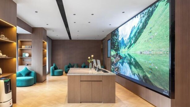 Un hall d’hôtel moderne doté d’un grand écran de télévision, d’un revêtement de sol en bois, de sièges de couleur turquoise et d’un îlot central.