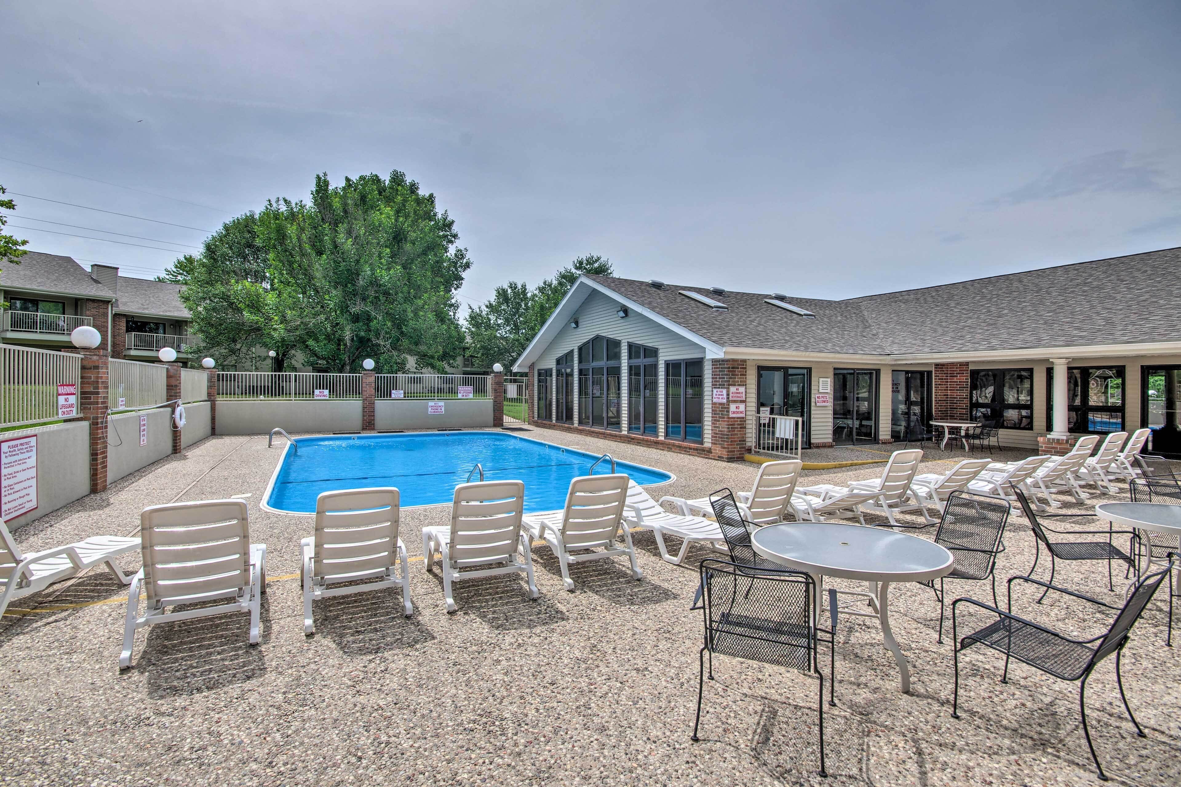 Un espace piscine doté de chaises longues et de tables, entouré d’un bâtiment avec un patio couvert.