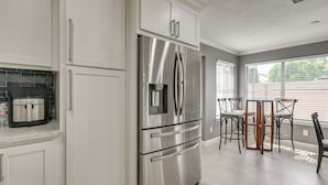 Une cuisine moderne avec des meubles blancs, un réfrigérateur en acier inoxydable, un four encastré et une machine à café posée sur le plan de travail.