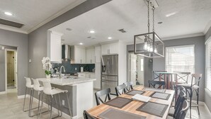 Une cuisine moderne avec des meubles blancs, des appareils en acier inoxydable et un îlot central doté de tabourets de bar.