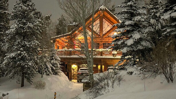 Una cabaña de troncos con fachada de madera, rodeada de árboles cubiertos de nieve.