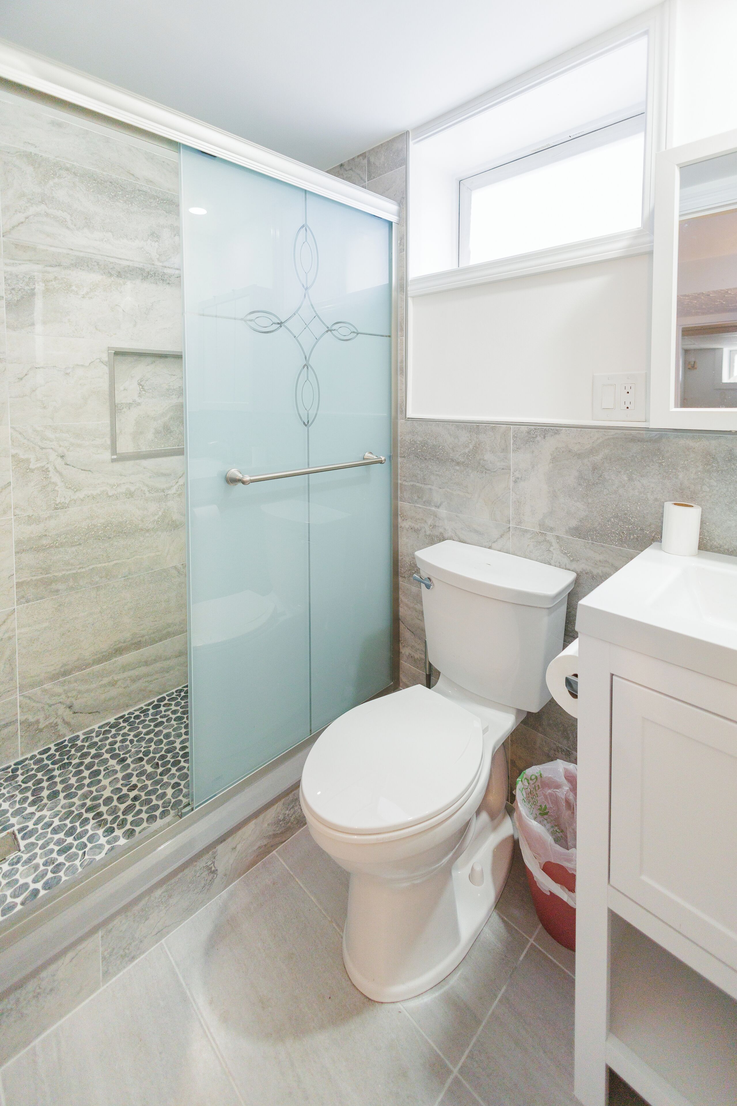 A bathroom with a glass shower enclosure, a toilet, and a sink.